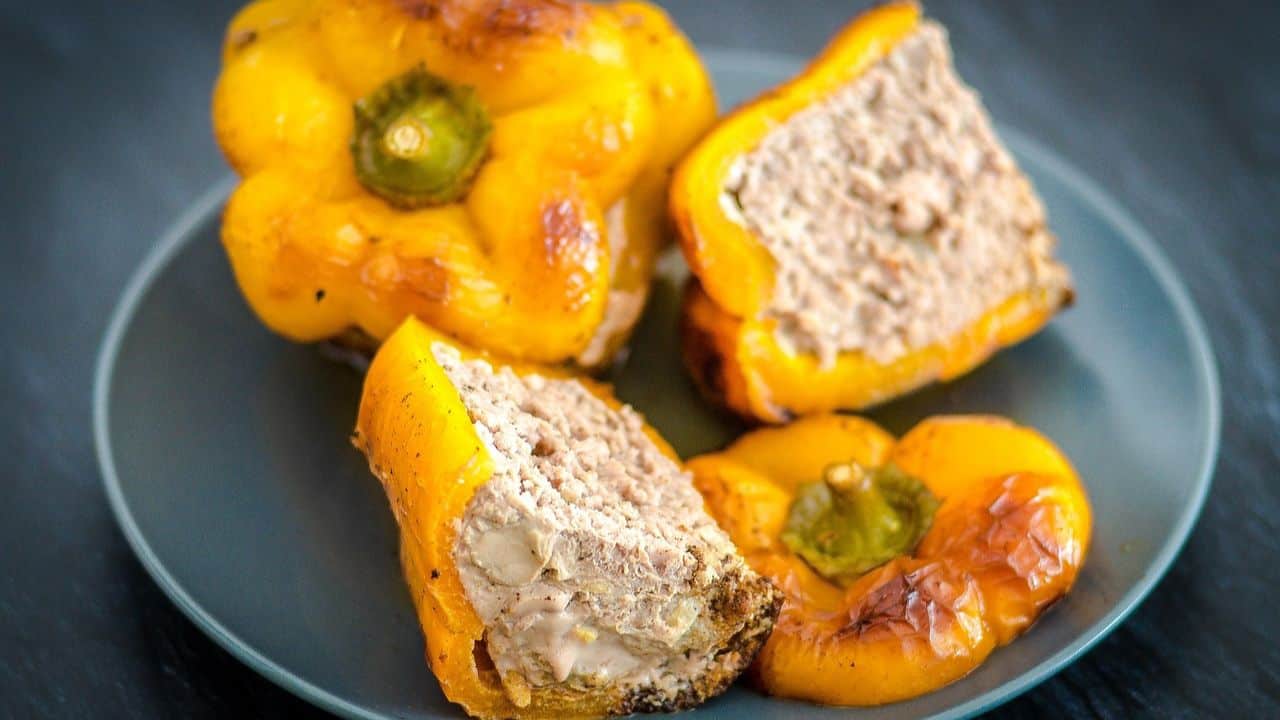 A blue plate with yellow bell peppers stuffed with a ground meat mixture, some whole and some sliced to show the filling.