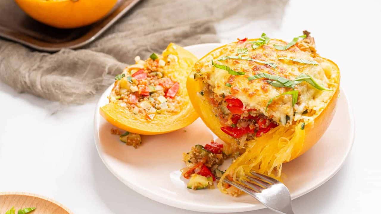 An image of two stuffed spaghetti squashes on a white plate with a fork slicing a part of one of the squashes.