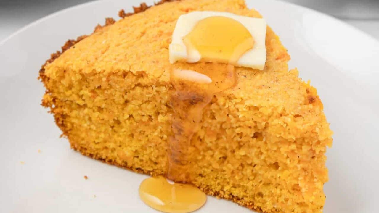 An image of a slice of sweet potato cornbread on a plate with butter and honey on top.