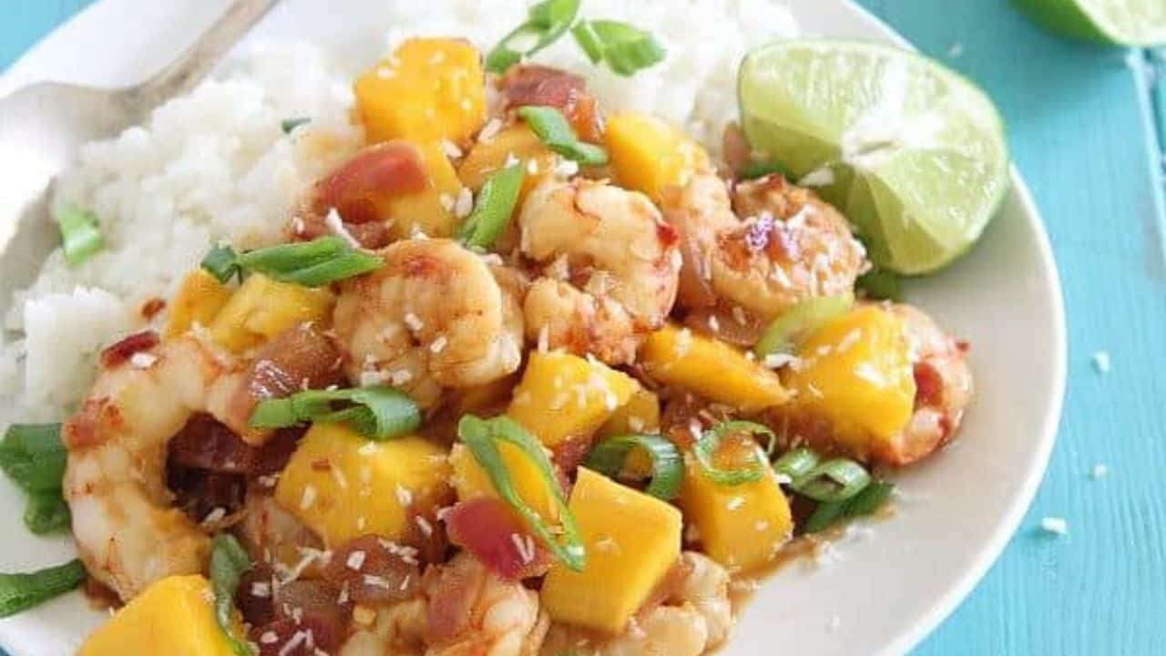 Mango shrimp served with white rice on a white plate with spoon.