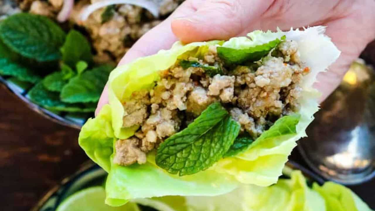 Low angle shot of a striped bowl filled with Thai larb salad garnished with shallot slices.