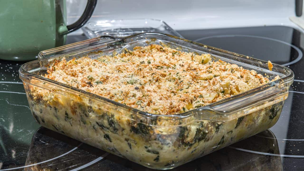 A glass baking dish filled with a baked casserole topped with golden breadcrumbs sits on a stove.