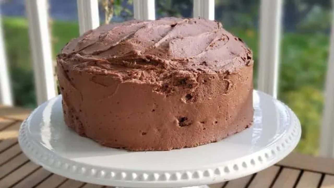Image shows a slice of chocolate frosted chocolate cake on a plate sitting on a wooden table.