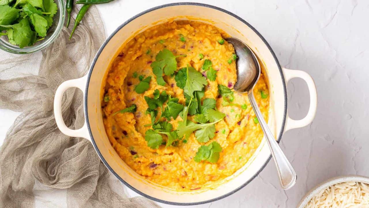 An overhead image of vegetable korma in a bowl, garnished with cilantro and with a spoon on the side.
