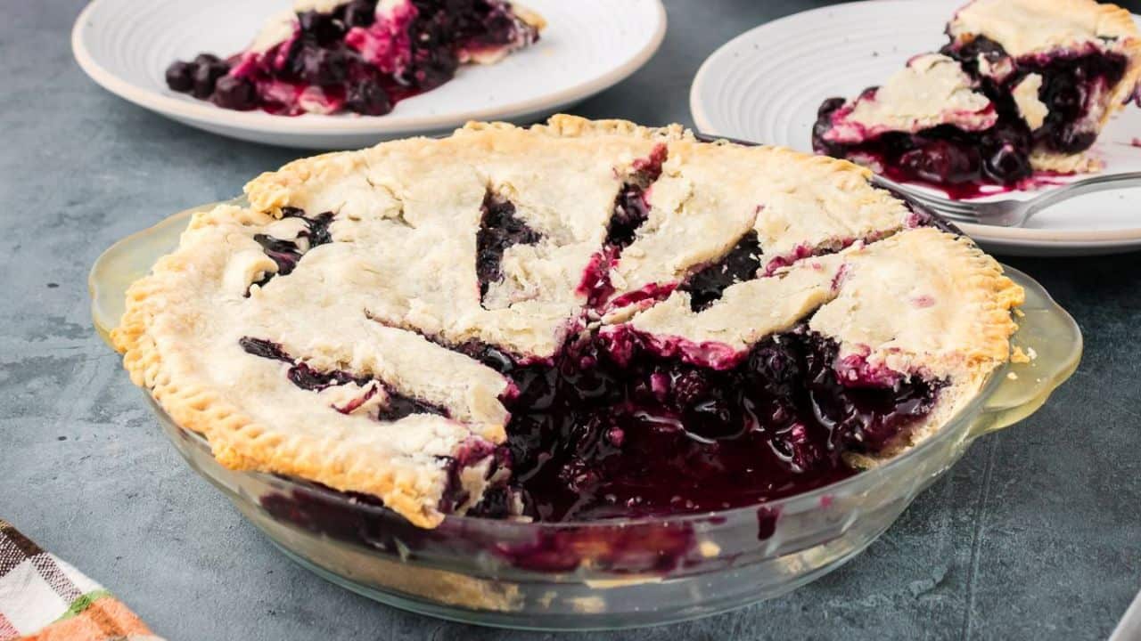 Slice of blueberry pie with whipped cream on glass plate.
