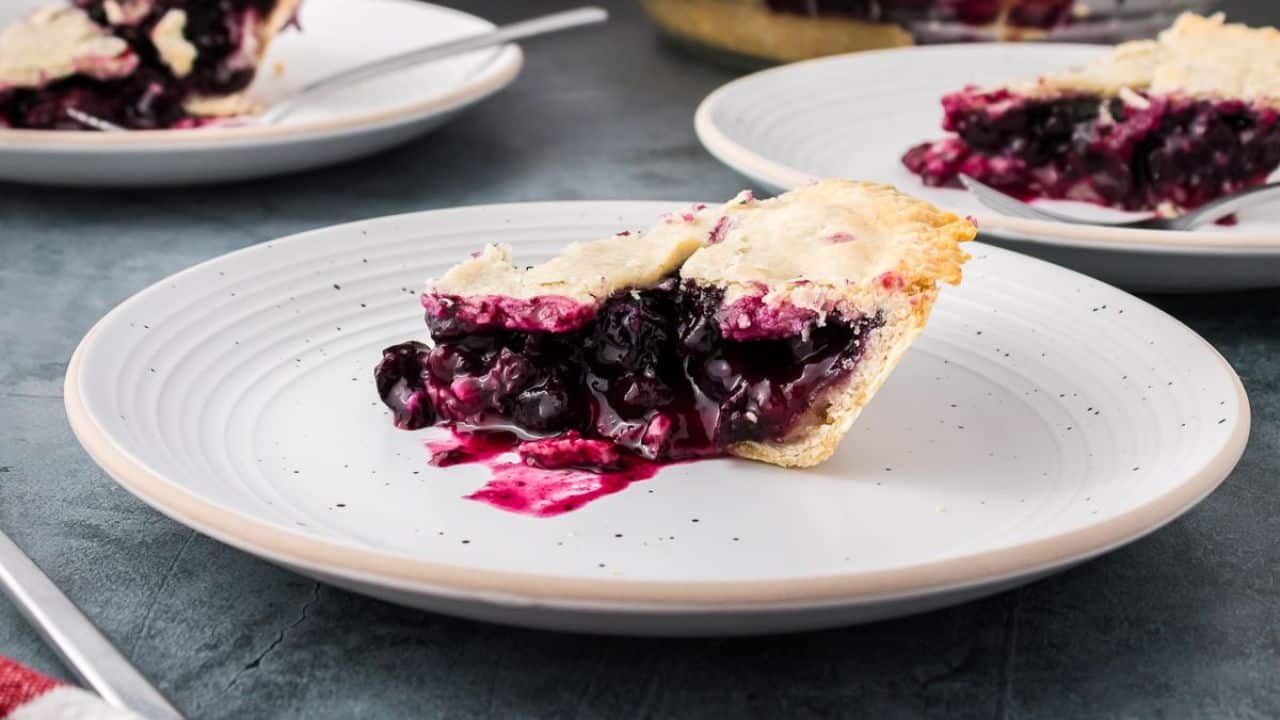 Slice of blueberry pie with whipped cream on glass plate.