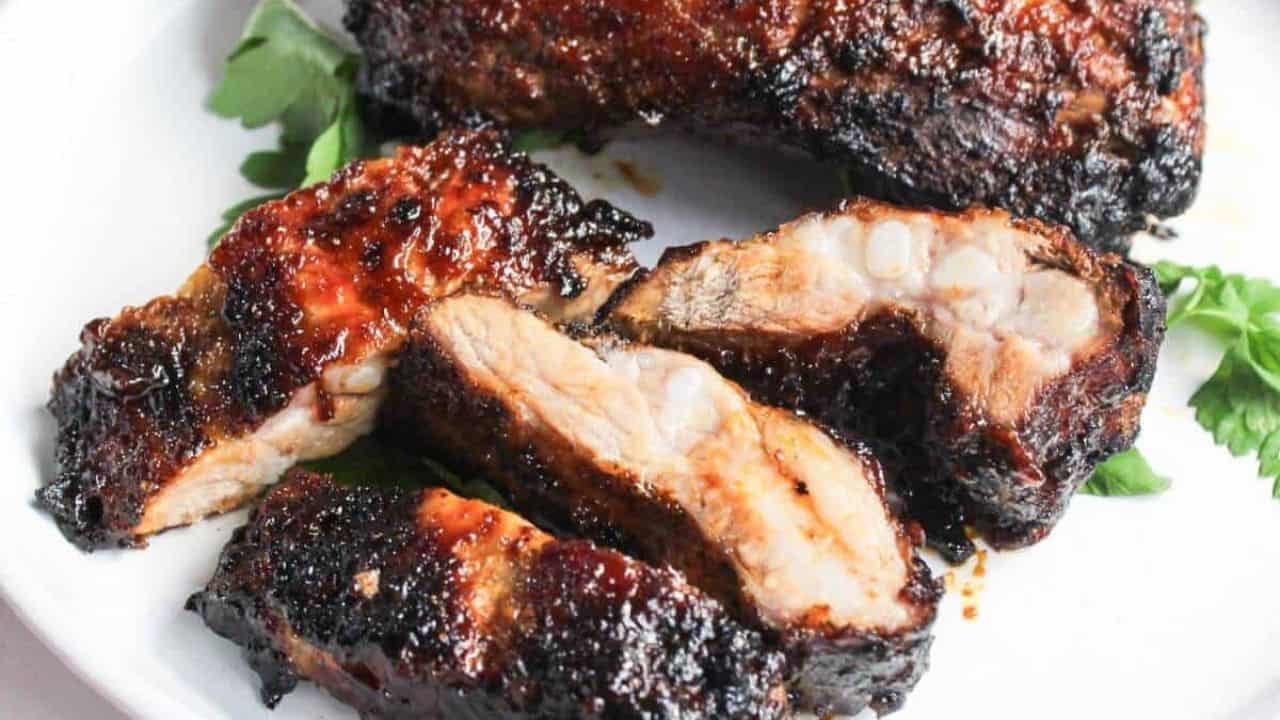 Close-up of an air-fried barbecued rib with charred edges over a white plate.