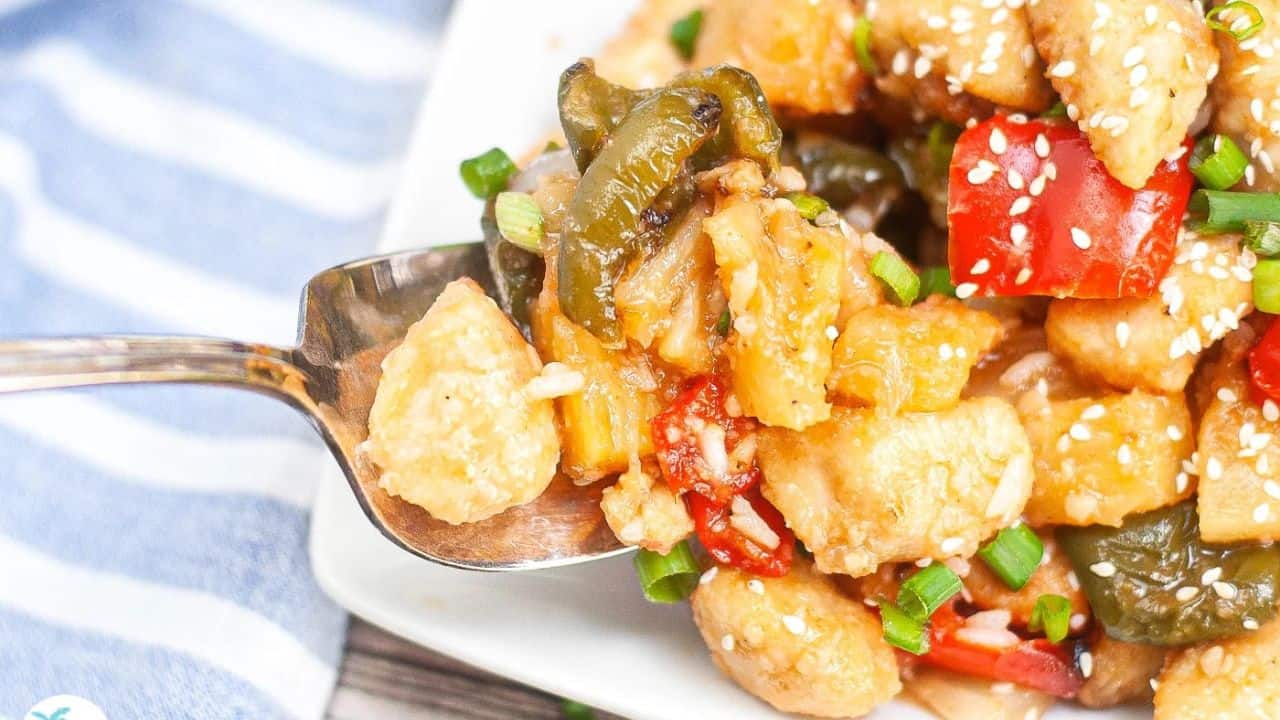 Sweet and sour chicken chunks in a glossy sauce, served on a white plate with garnish.
