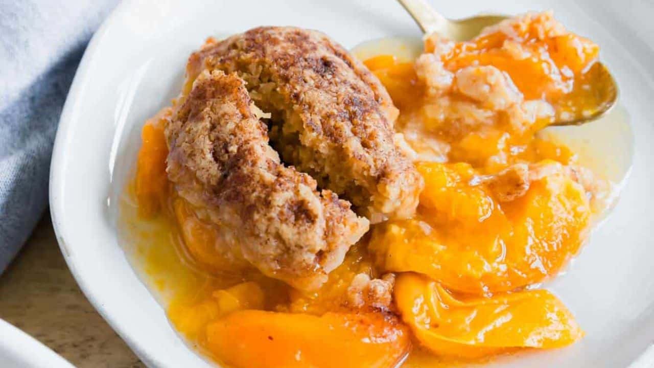 Apricot cobbler in a white baking dish with wooden metal serving spoon on a wooden surface.