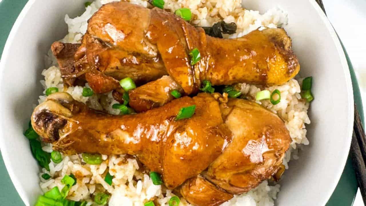 A plate of brasied chicken legs served with rice, accompanied by a pair of chopsticks resting on the side.