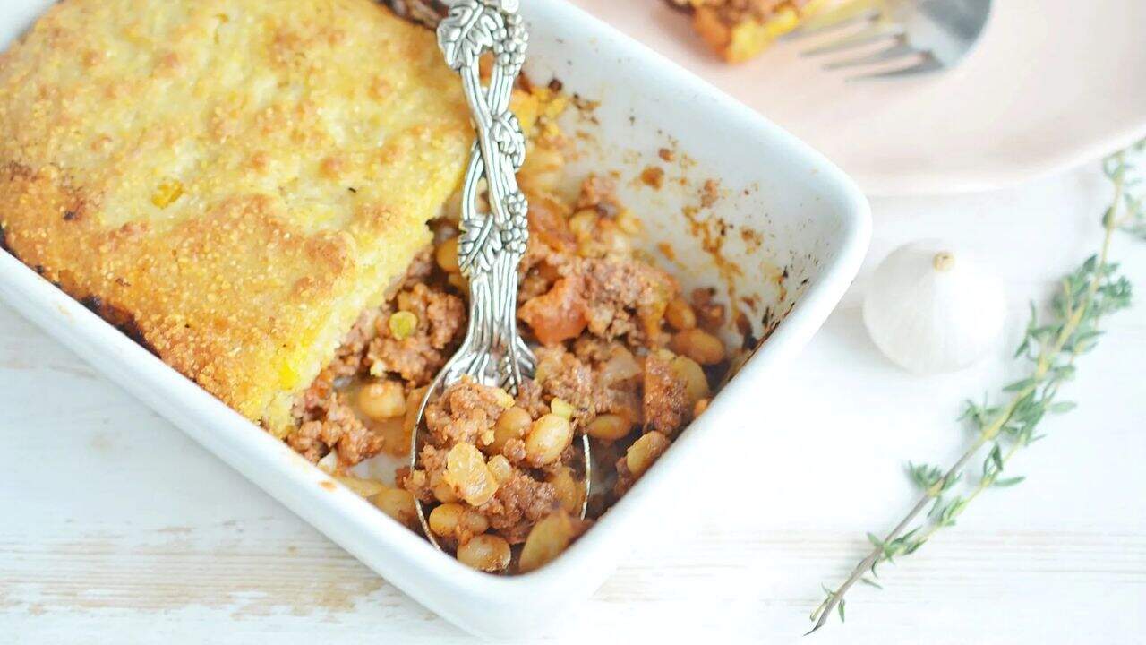 A white casserole dish with cornbread casserole and a silver serving spoon.