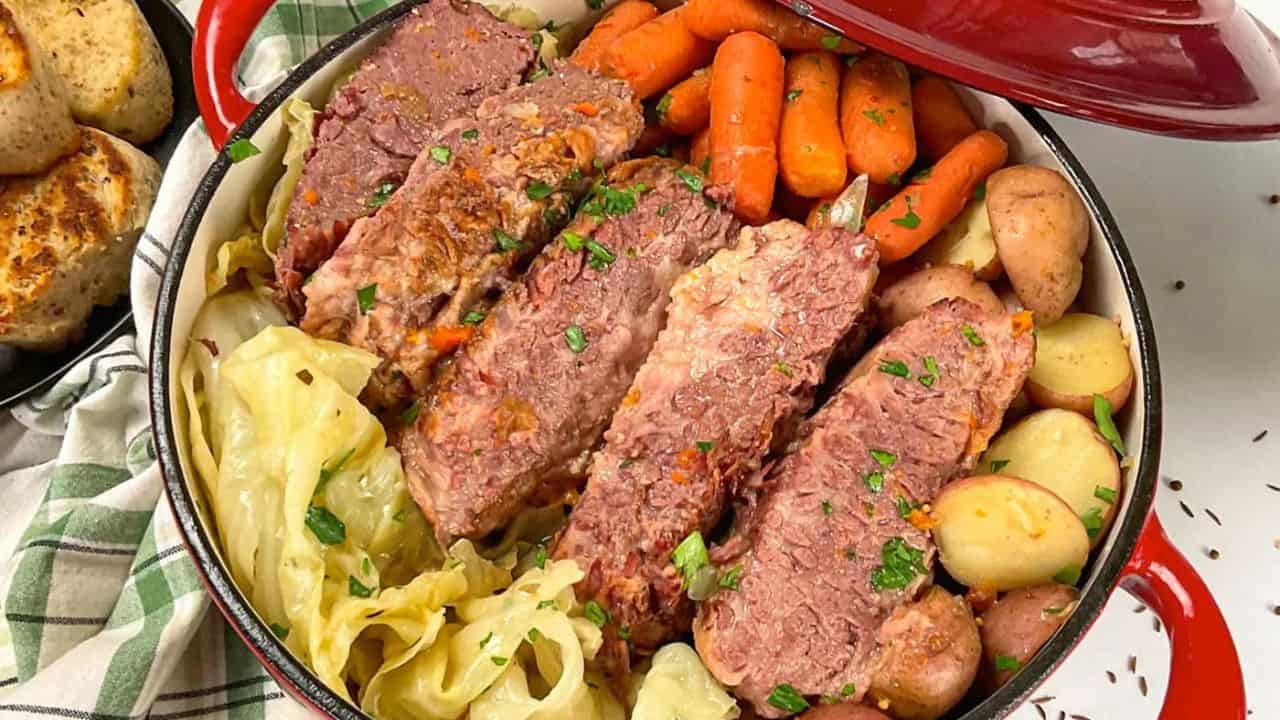 A pot filled with slices of corned beef, baby carrots, halved potatoes, and cooked cabbage, garnished with chopped parsley.