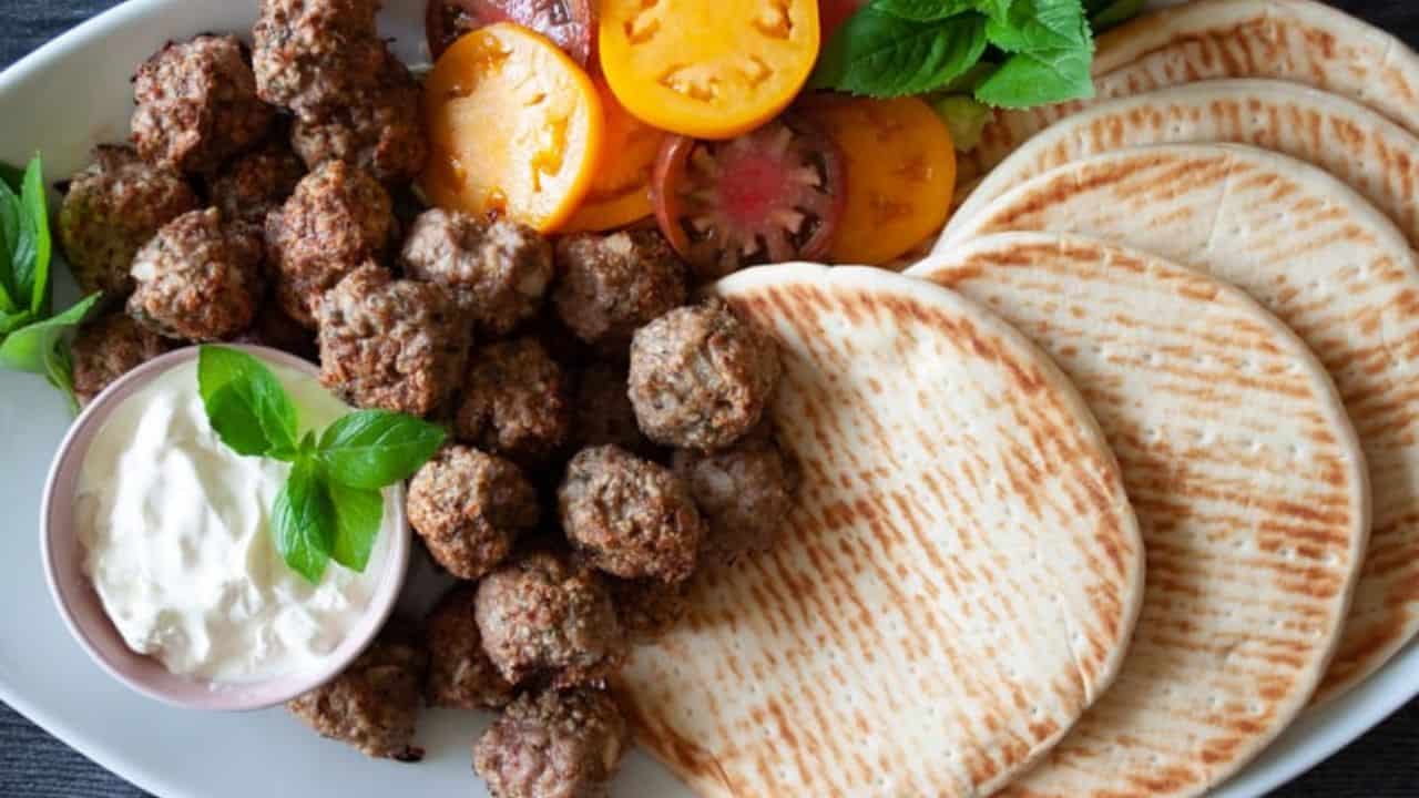 Baked turkey meatballs with tomato slices, pita bread, dipping sauce, and fresh mint.