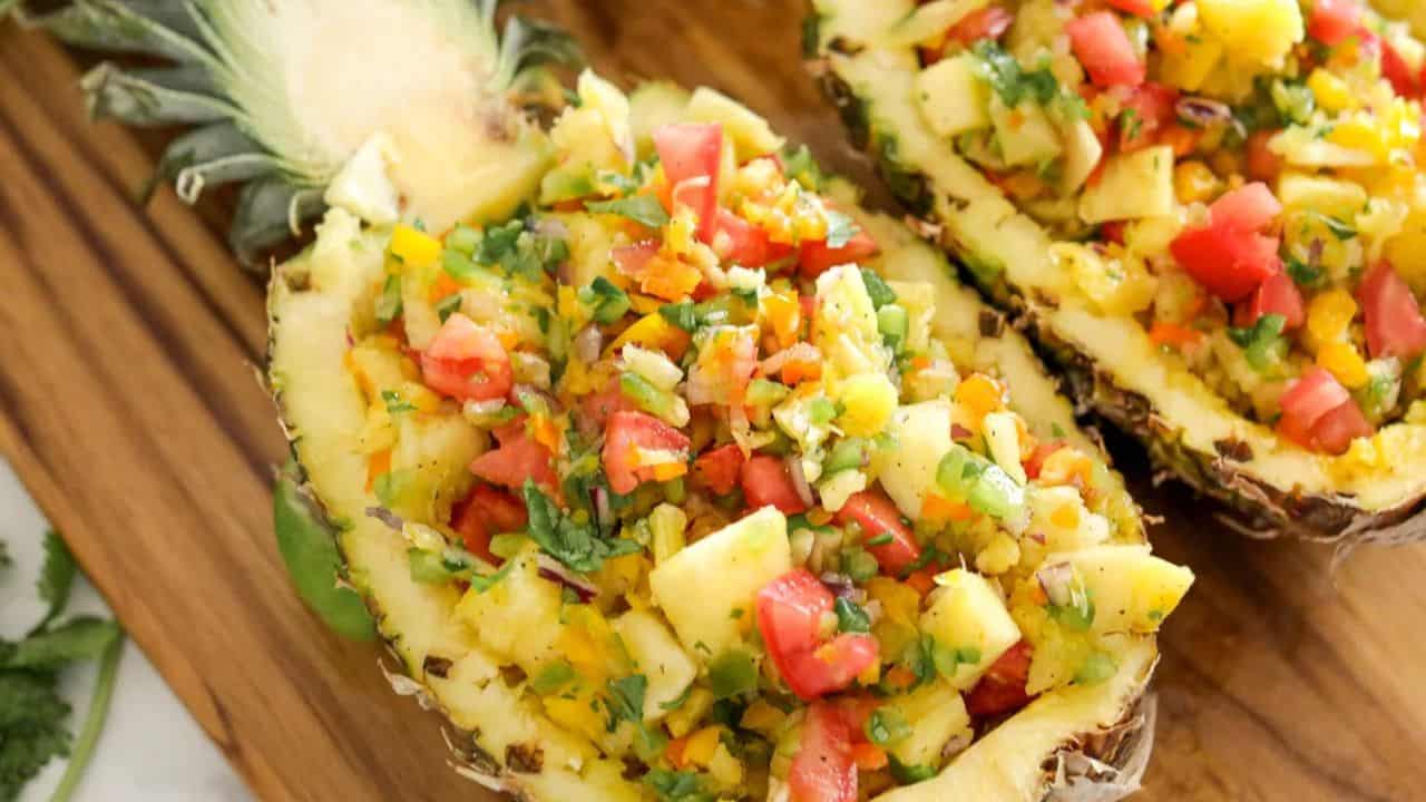 Two pineapple halves filled with chopped vegetables and pineapple pieces, presented as decorative serving bowls on a wooden surface.