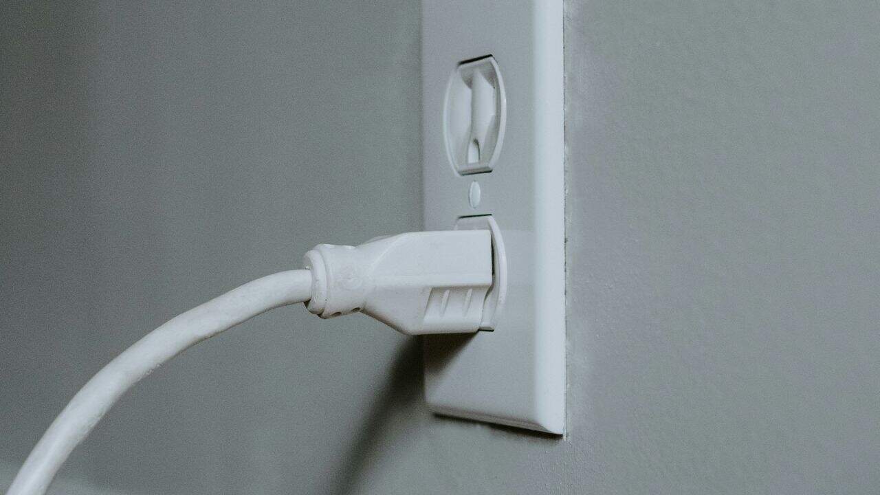A white electrical plug is inserted into a white wall outlet near a light gray wall.