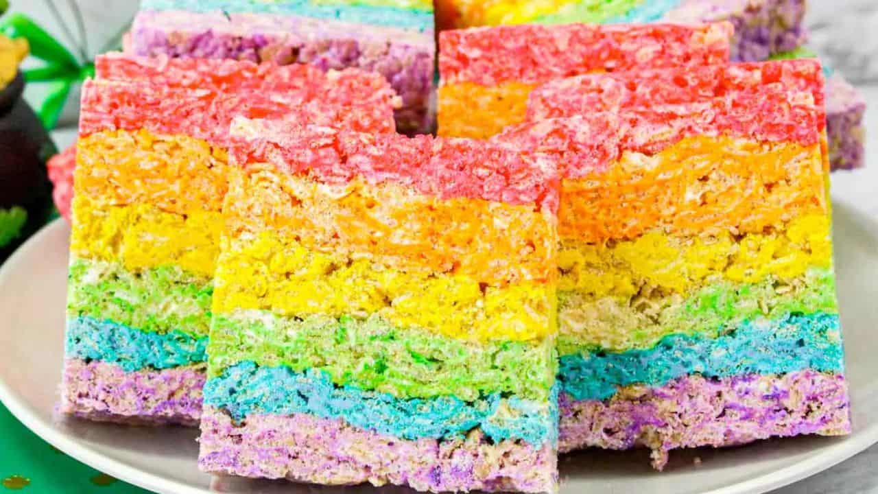 A plate of rainbow-colored rice crispy treats stacked in layers of red, orange, yellow, green, blue, and purple.