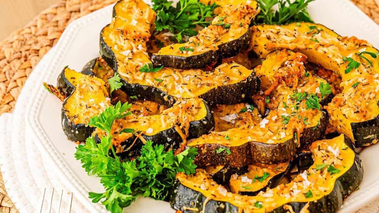 Sliced roasted acorn squash garnished with fresh parsley and shredded cheese, served on a white plate.