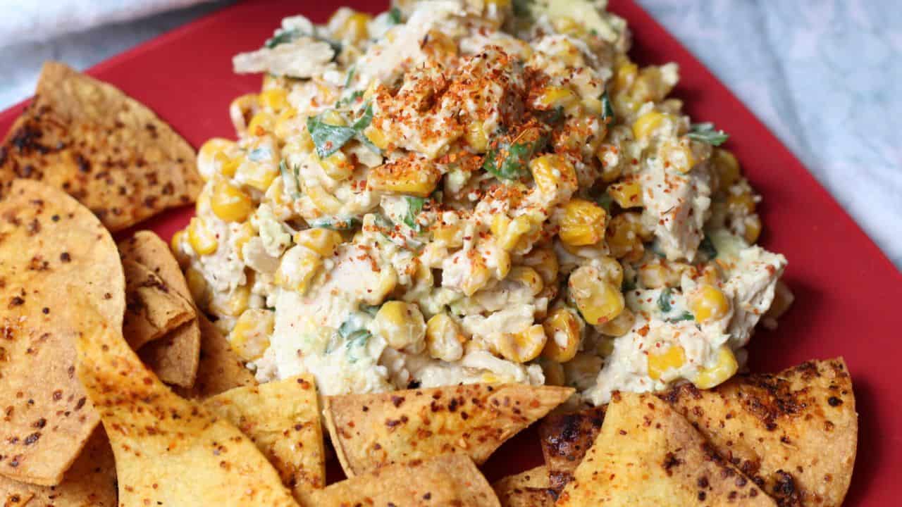 Red plate with chicken salad and chips.