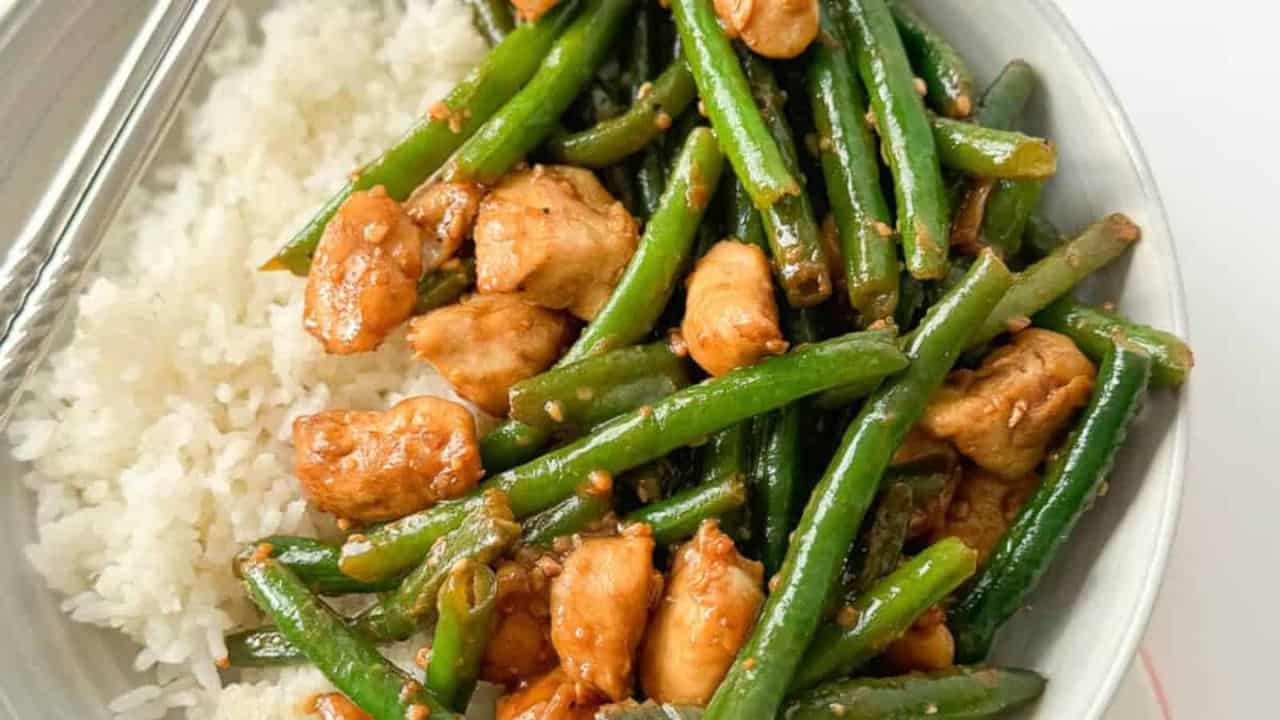 A colorful stir-fry dish of chicken and string beans stir-fried together on a white plate.