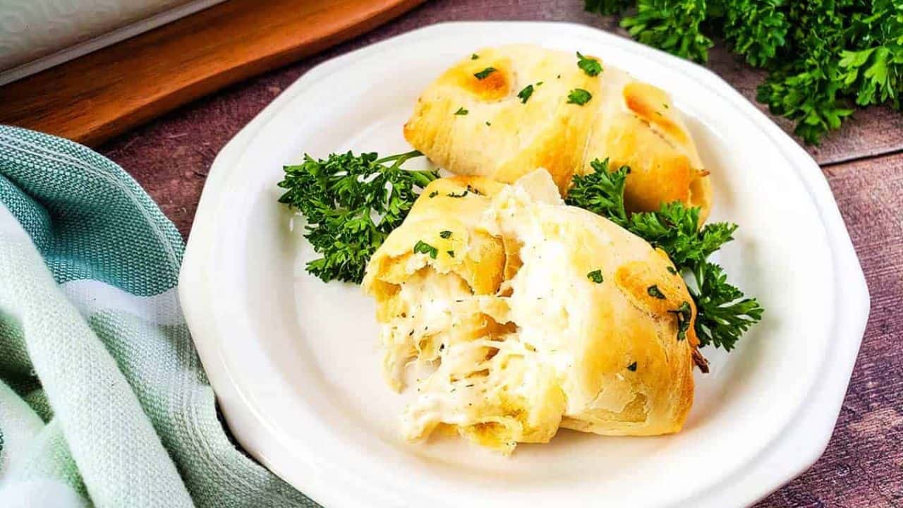 Front view of 2 stuffed chicken Crescent rolls on a white plate garnished with parsley.