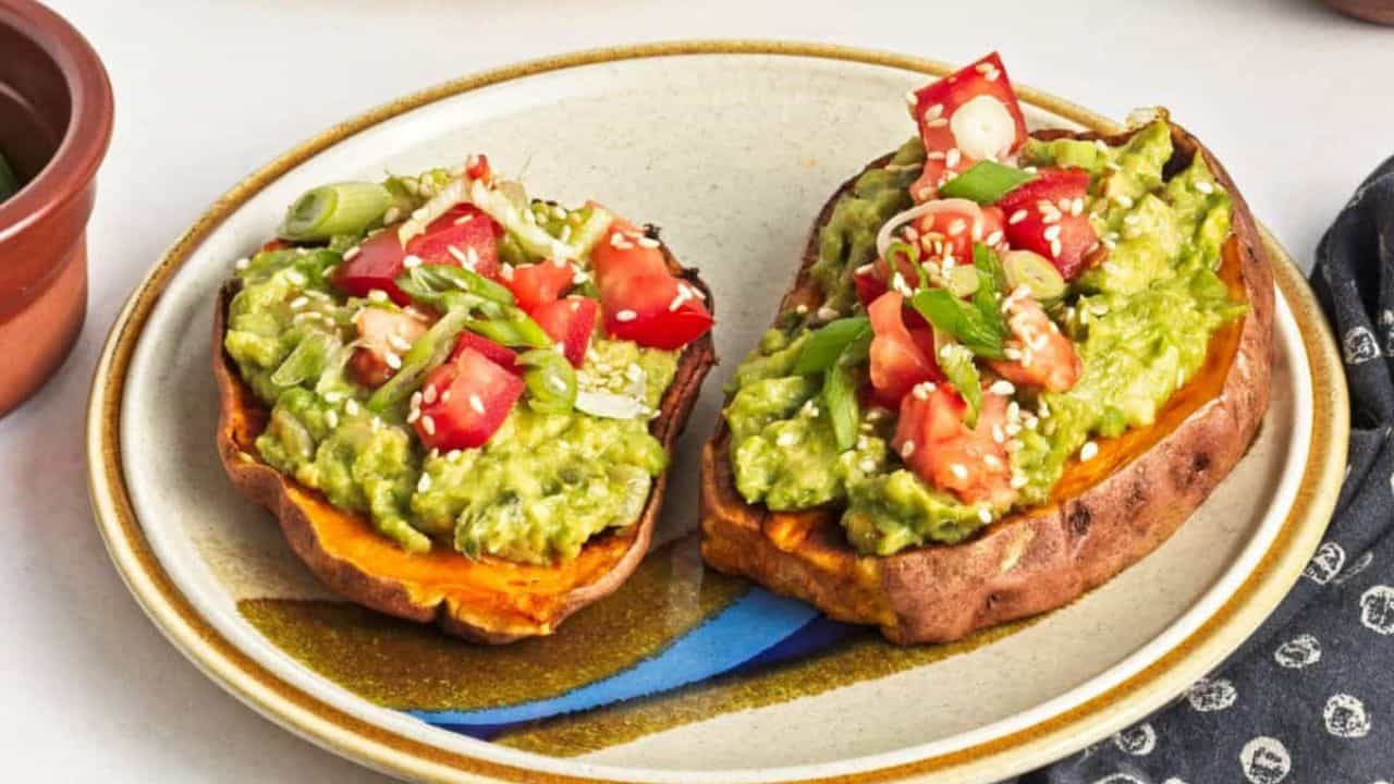 A plate of sweet potato avocado toasts garnished with diced tomatoes and seeds, served with lemon and avocado halves.
