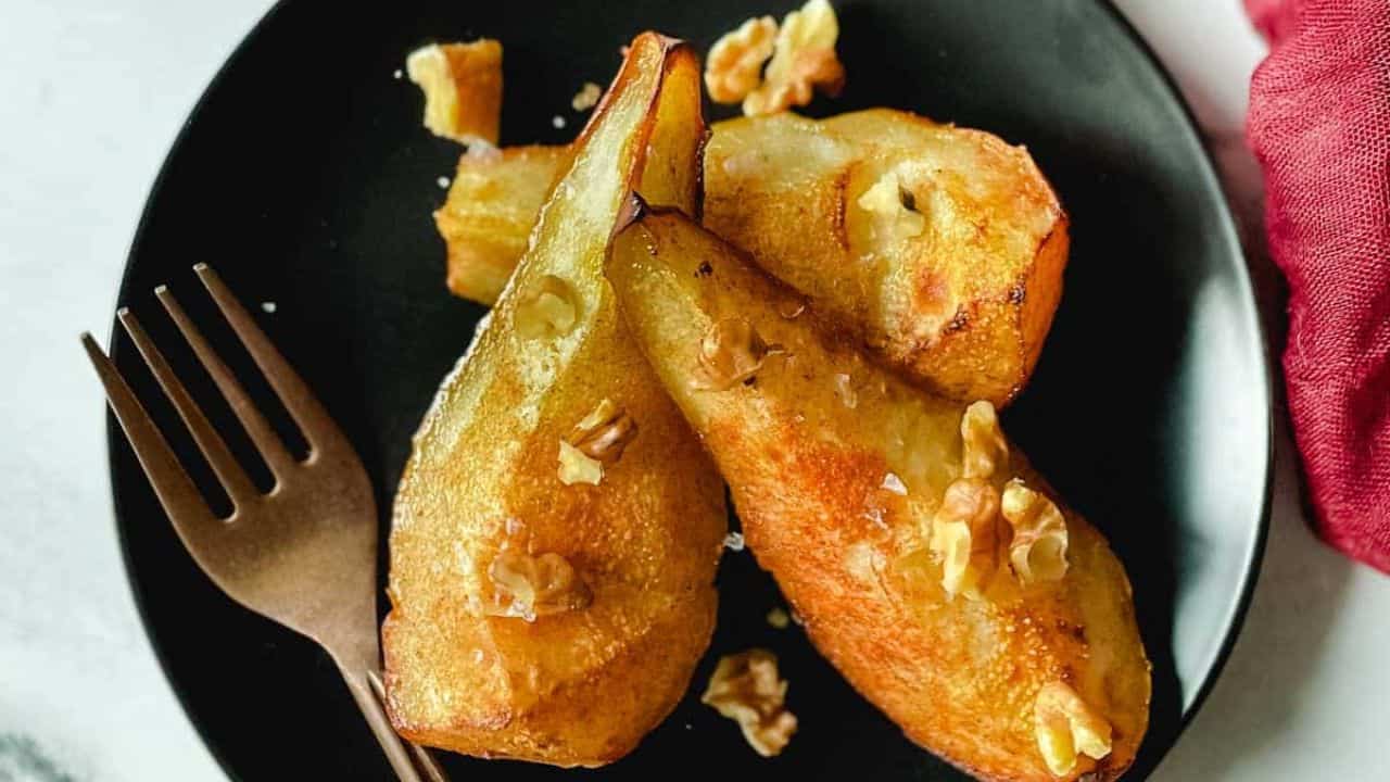 Air fryer pears sit on a black plate topped with walnuts.