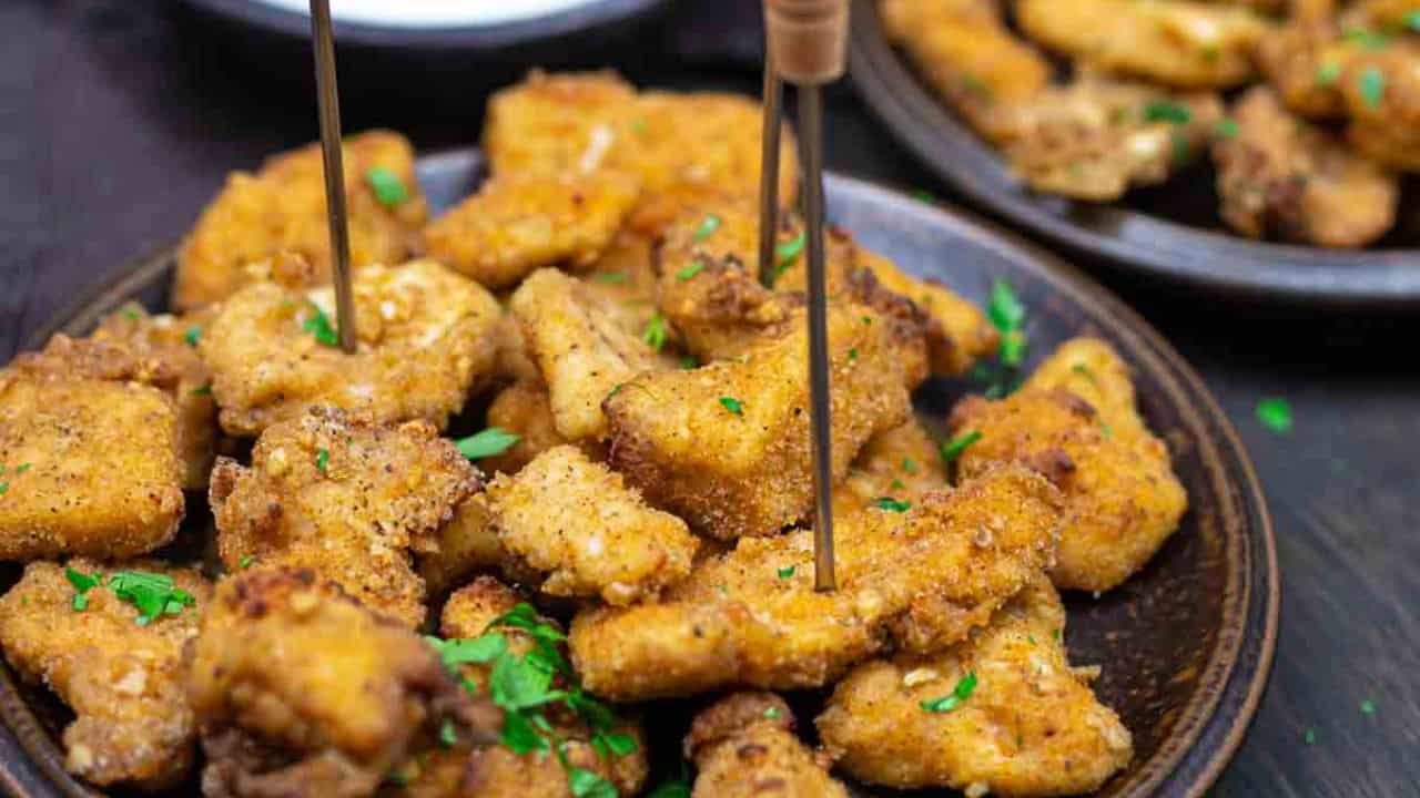 Plates of breaded and fried chicken nuggets with skewers, garnished with herbs.