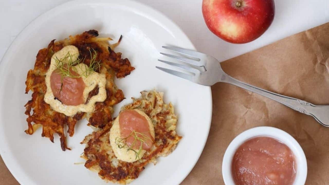 Apple potato latkes with curried yogurt sauce and applesauce on a white plate.