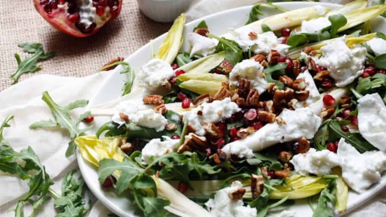 Side view of arugula salad on platter with pomegranates.
