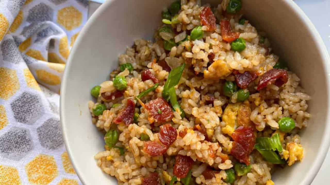 Bacon fried rice in a white bowl with green onions on the top.