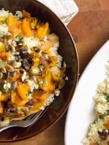 A bowl and a plate of couscous topped with roasted squash, caramelized onions, herbs, pumpkin seeds, and a sprig of rosemary on the side.