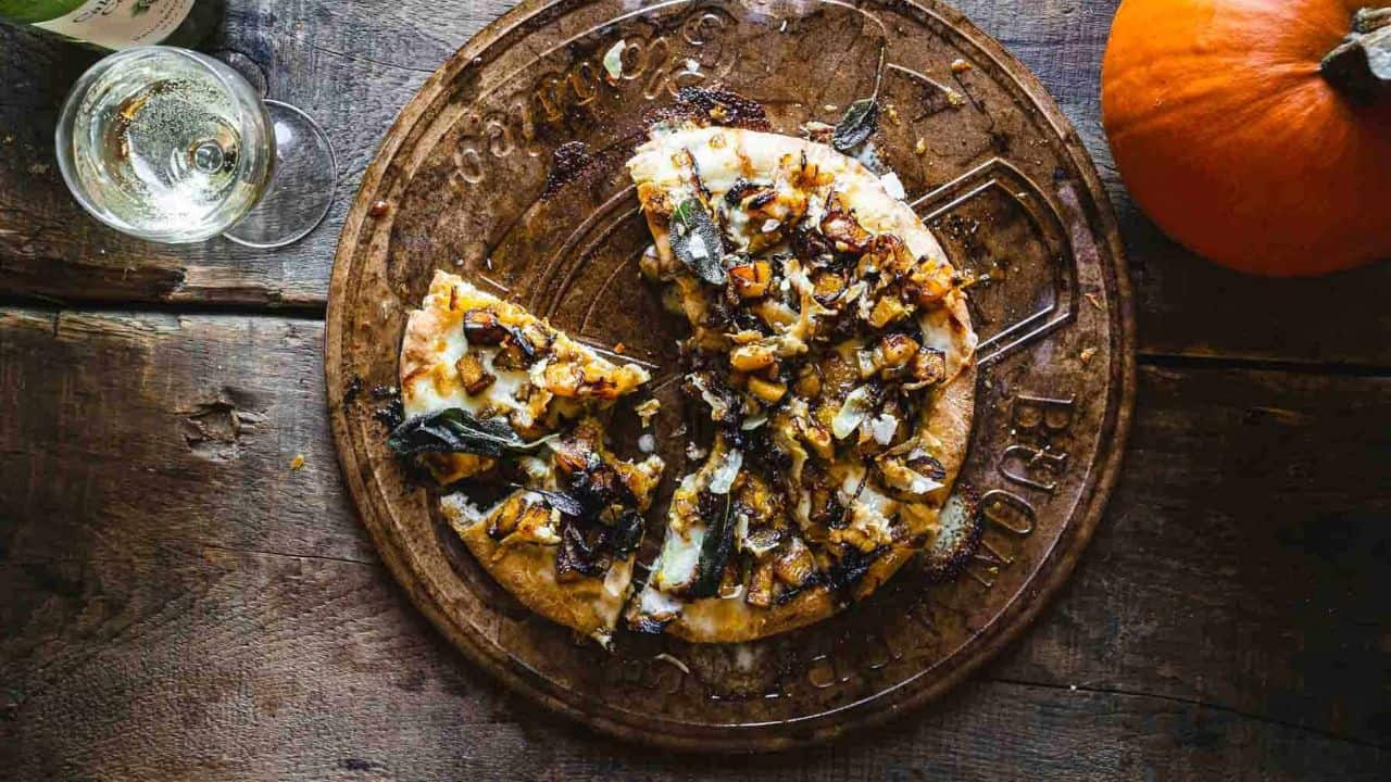 A vegetarian pizza topped with onions and sage, served on a rustic wooden board.