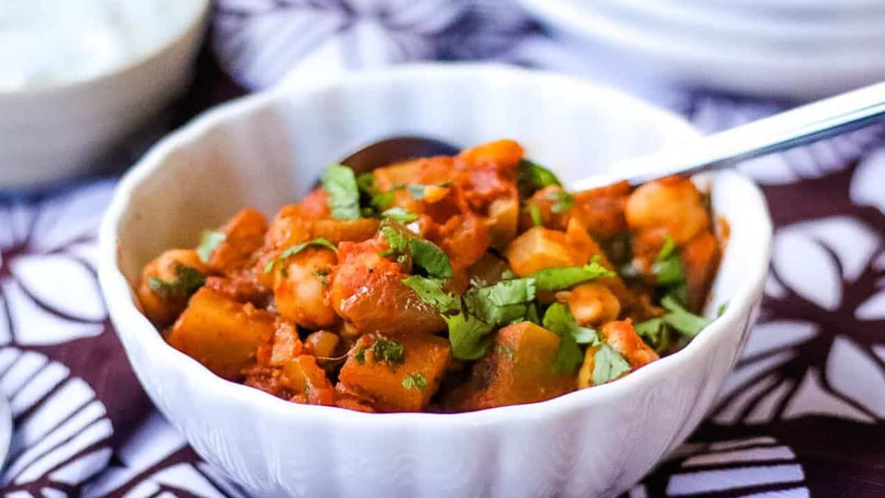 Chana aloo masala in a white bowl with a spoon, on top of a brown and white linen.