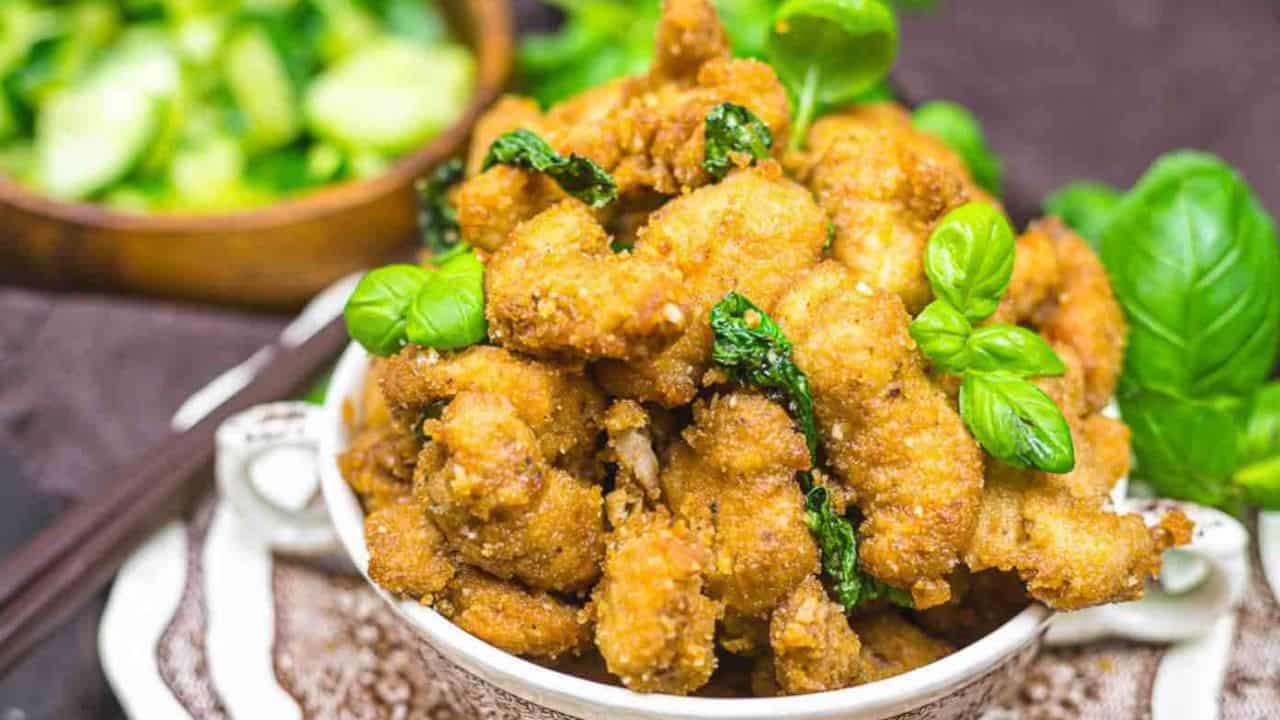 A bowl of crispy fried chicken garnished with basil leaves.