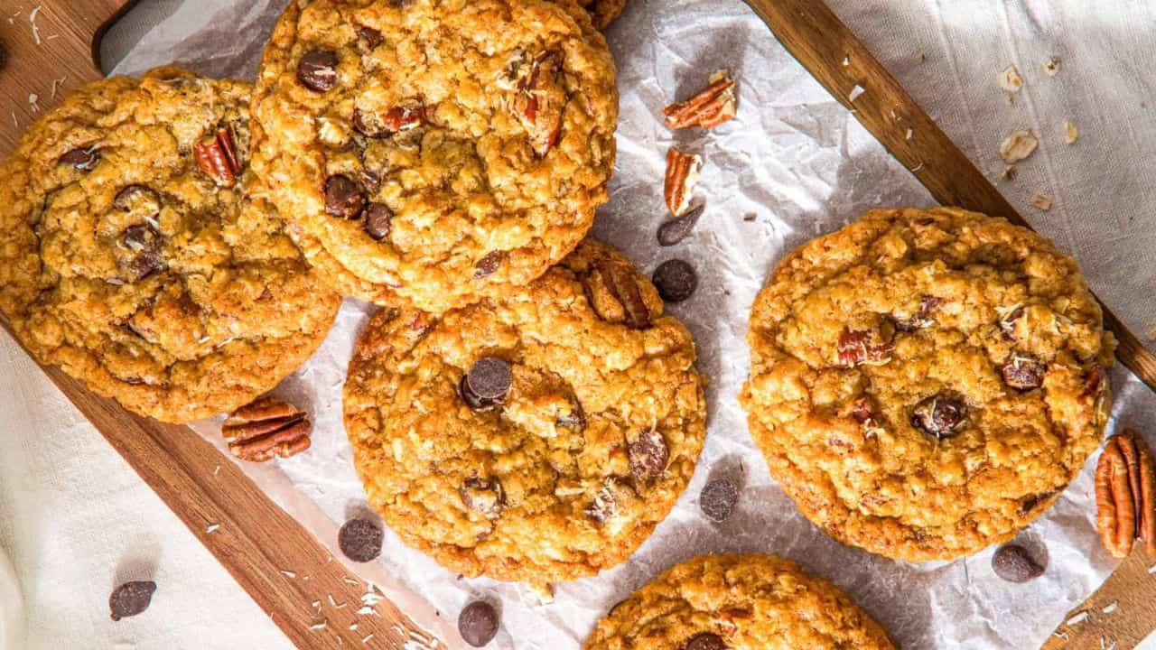 A close up image of a stack of cowboy cookies arranged on a serving platter with a glass of milk at the back.