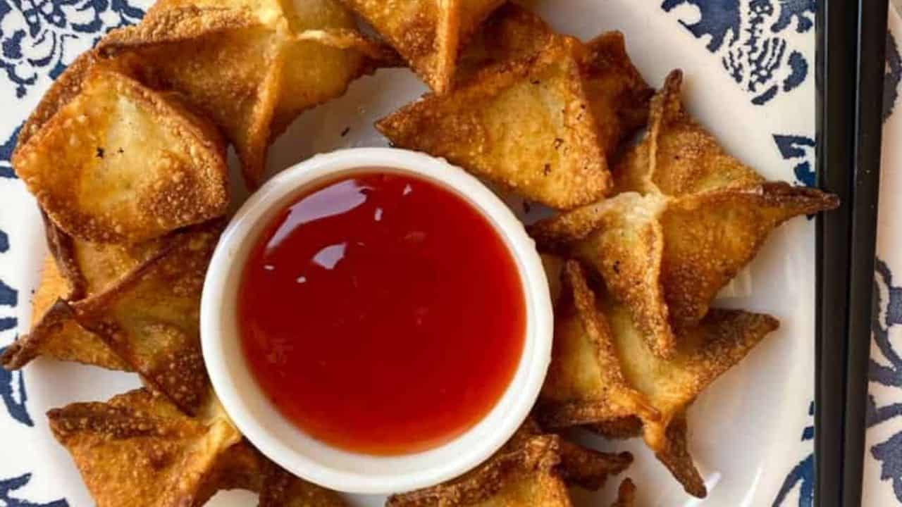 Crispy fried wontons stuffed with creamy crab and cream cheese filling on a blue-white plate.
