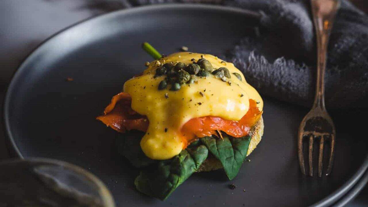 A person holding an eggs benedict with salmon and capers on a plate.