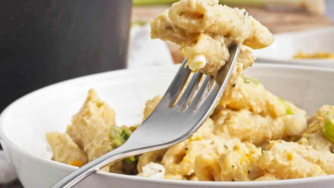 A bowl of creamy penne pasta with a fork, placed on a textured surface.