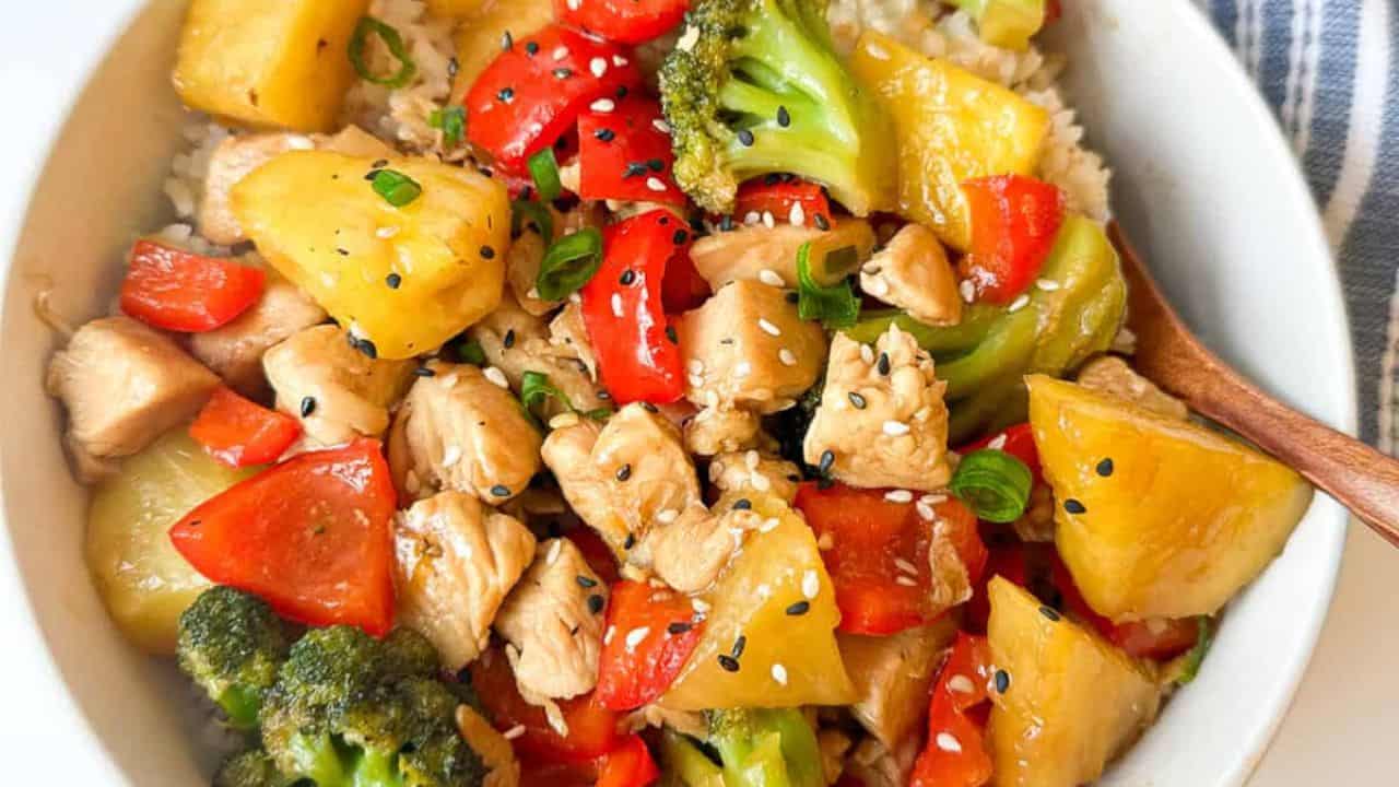A vibrant bowl containing chicken, assorted vegetables, pineapple chunks, teriyaki sauce, and rice.