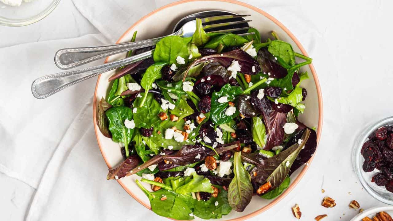 An image of cranberry salad with pecans served in a white salad bowl with a fork on the side.