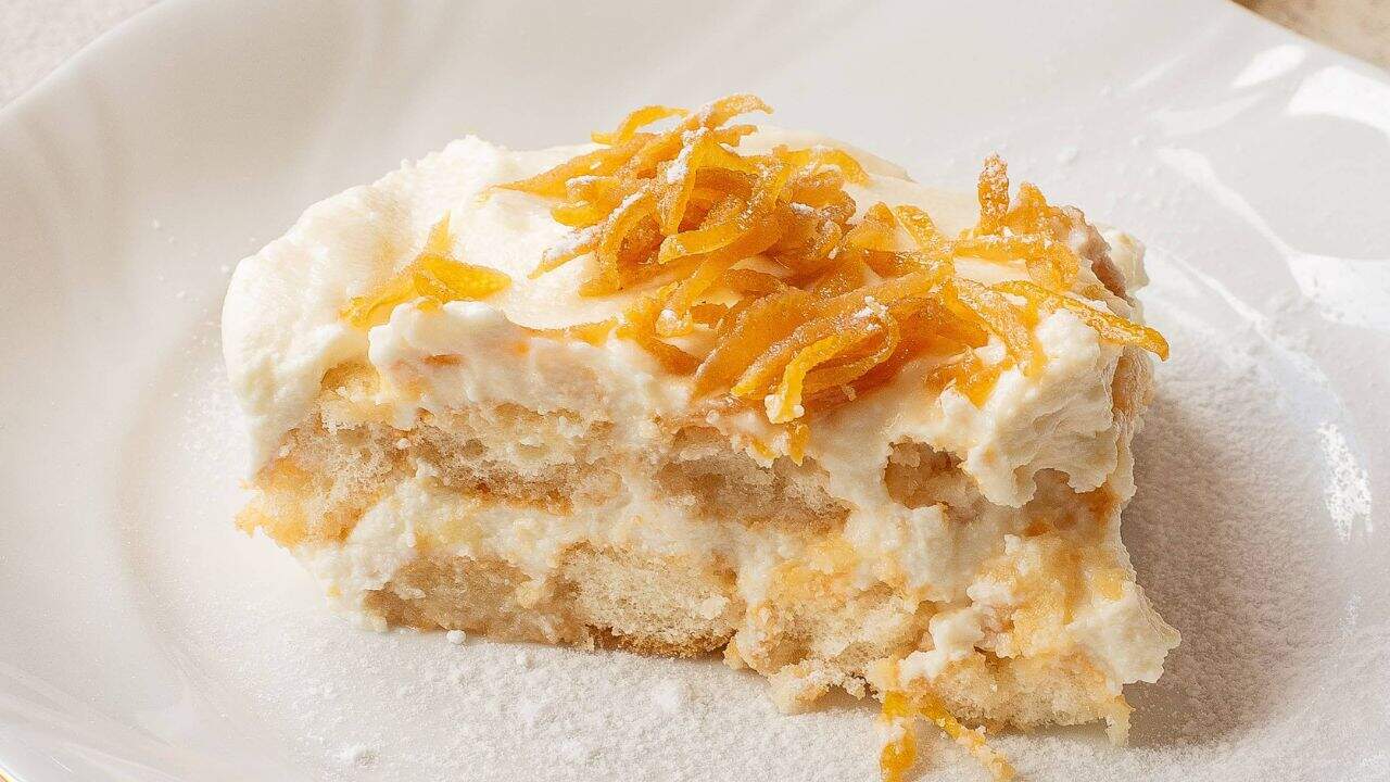 A slice of creamy tiramisu topped with shredded orange zest on a white plate.