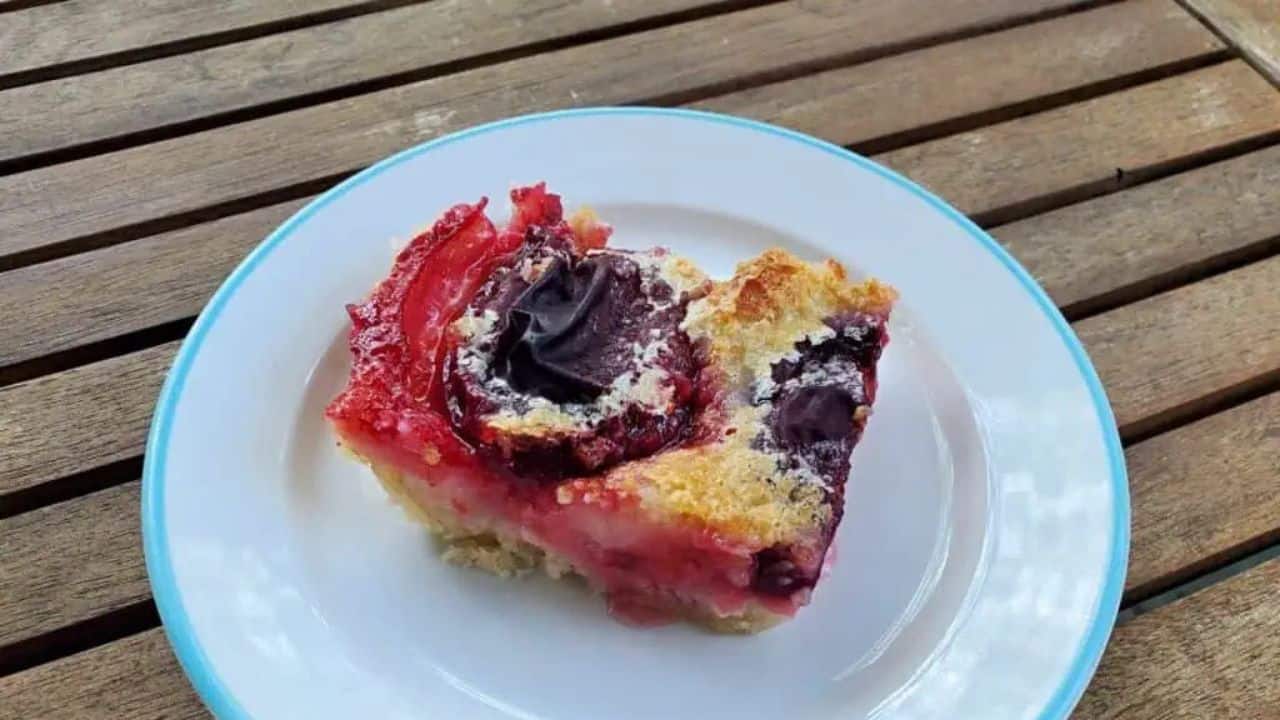Image shows an overhead shot of German Plum Kuchen in a blue pyrex pan on a wooden table.