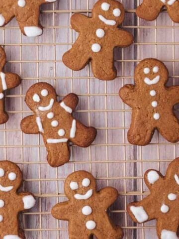 A cooling rack holding several gingerbread cookies shaped like people, decorated with white icing faces, buttons, and details.