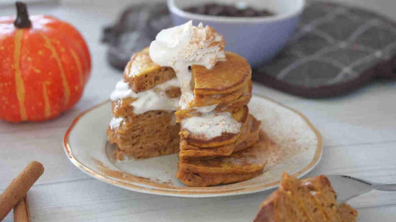 A stack of pumpkin pancakes with whipped cream and pecans.