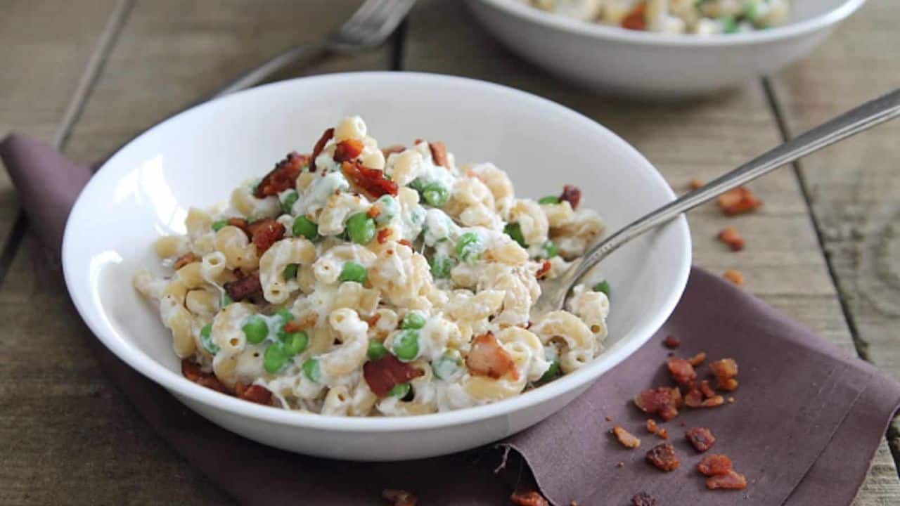 Greek yogurt mac and cheese with peas and bacon in a white bowl.