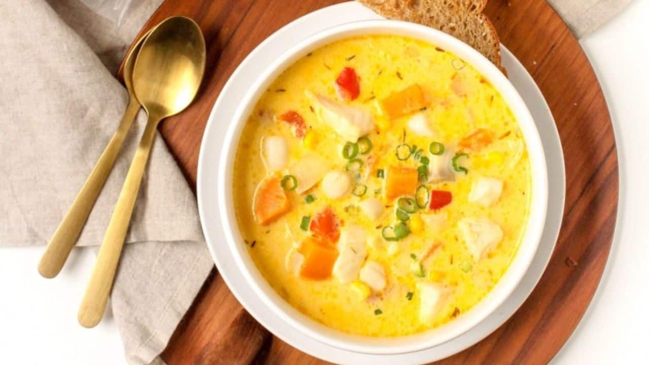 A bowl of seafood chowder with a spoon being held above it.