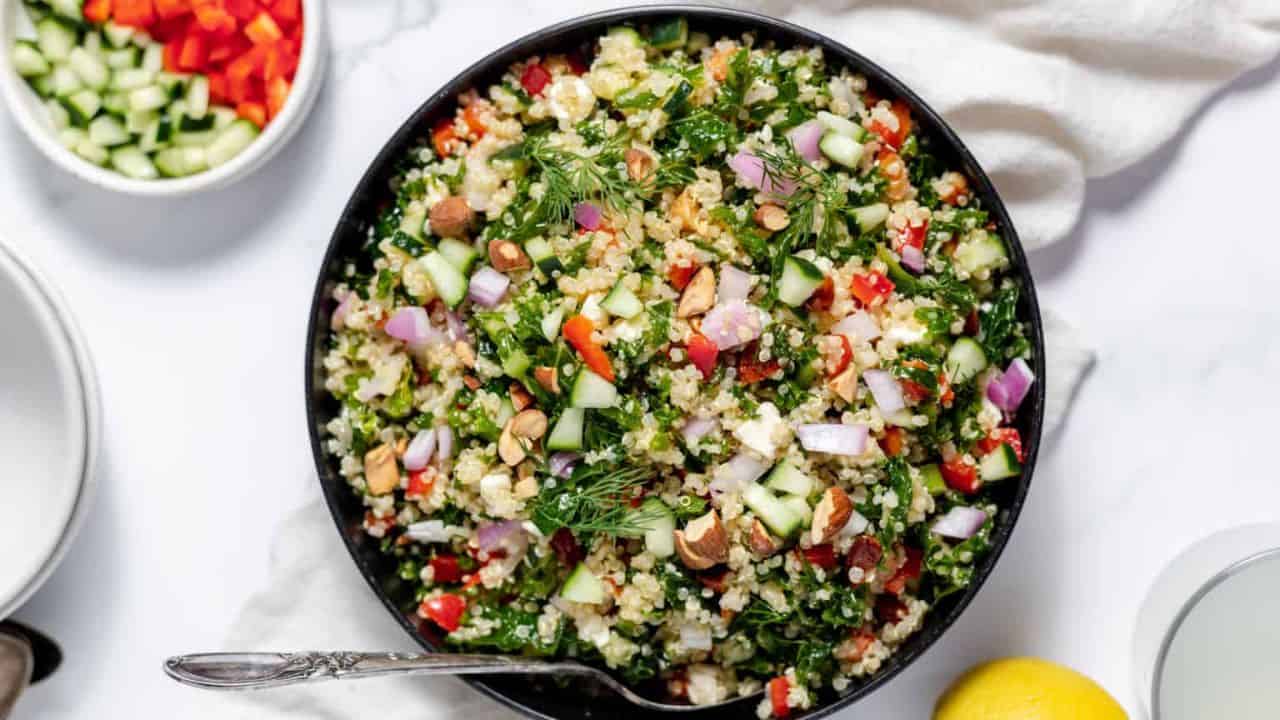 A bowl of kale quinoa salad with fresh sliced lemons and dill wids in the background.