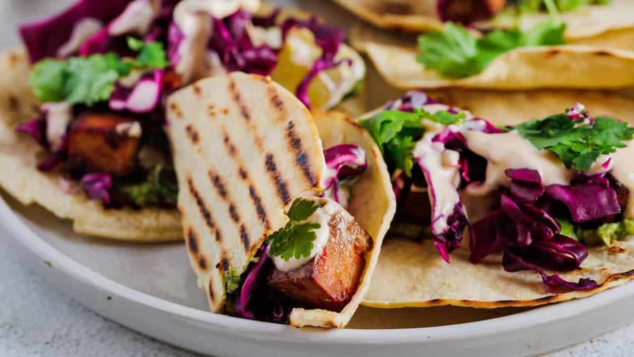 Side view of tacos on a plate, one with bite taken out.