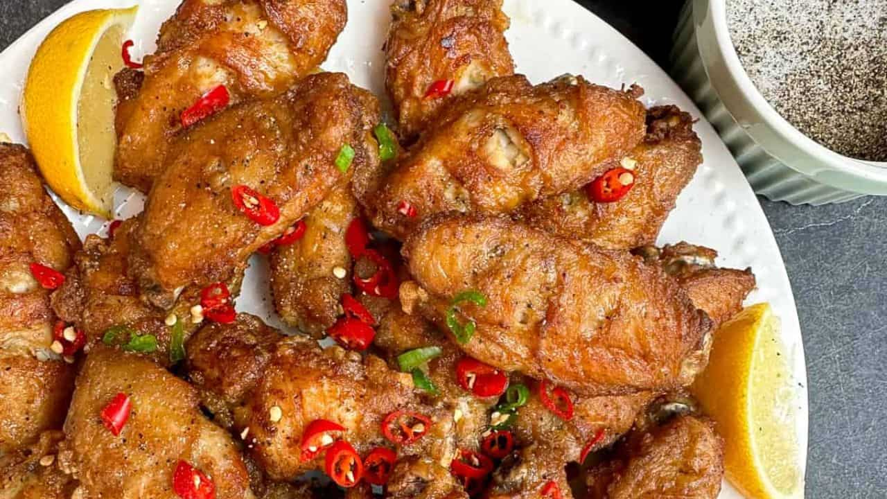 Crispy and flavorful salt and pepper chicken wings on a plate with lemon wedges.