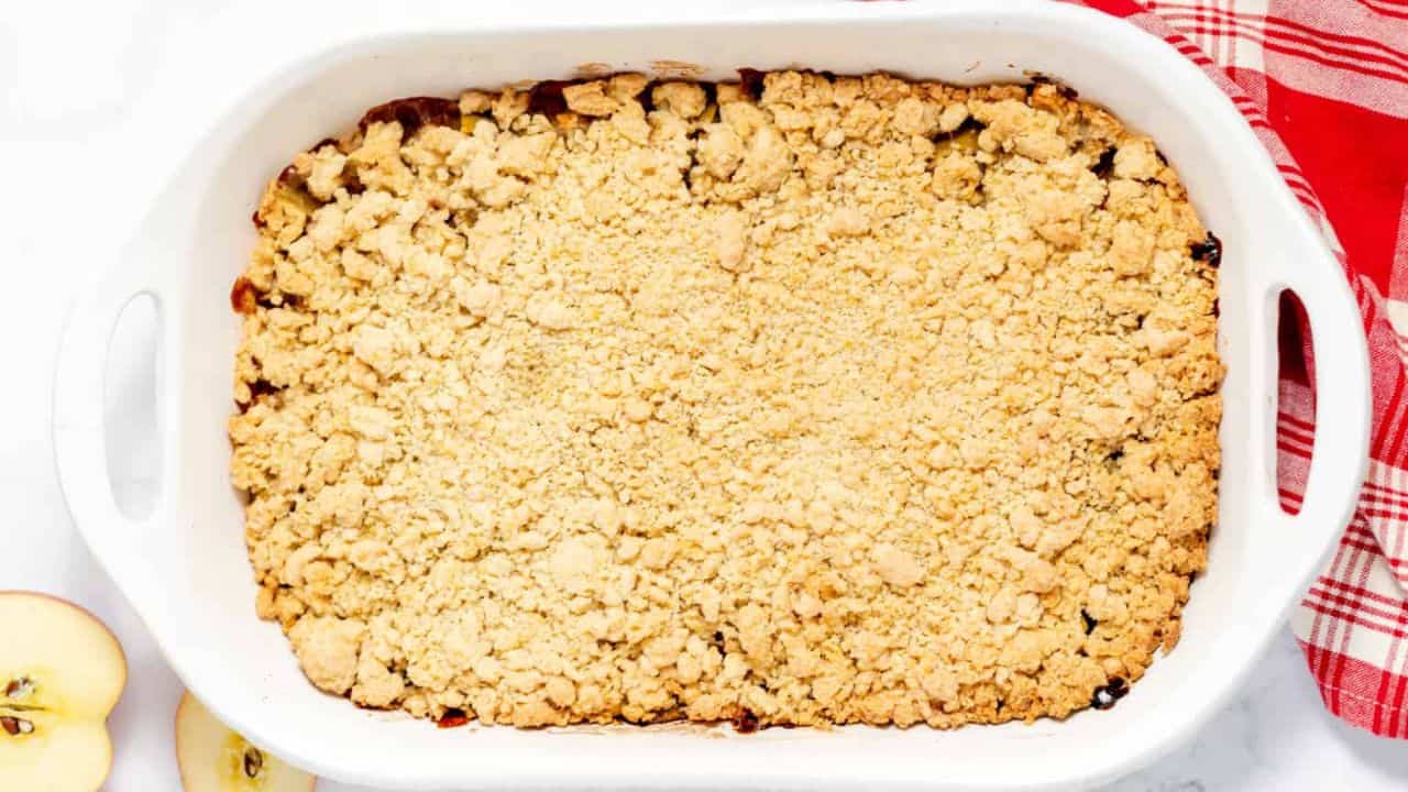 Apple crumble in a bowl with fresh apples in the background.